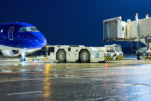 Le tracteur de remorquage fait reculer l'avion de passagers du pont aérien sur le tablier de l'aéroport de nuit