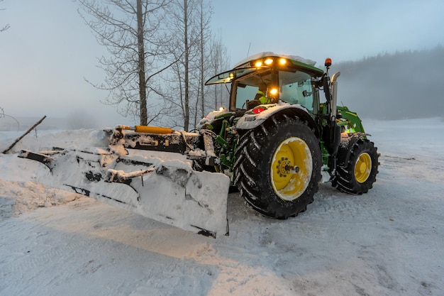 Tracteur vert enlevant la neige de la route avec la pelle pleine de neige et de glace et les lumières