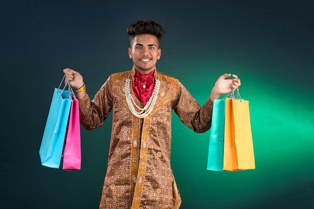 Photo traditionnel indien jeune homme beau tenant et posant avec des sacs d'achat sur un fond sombre