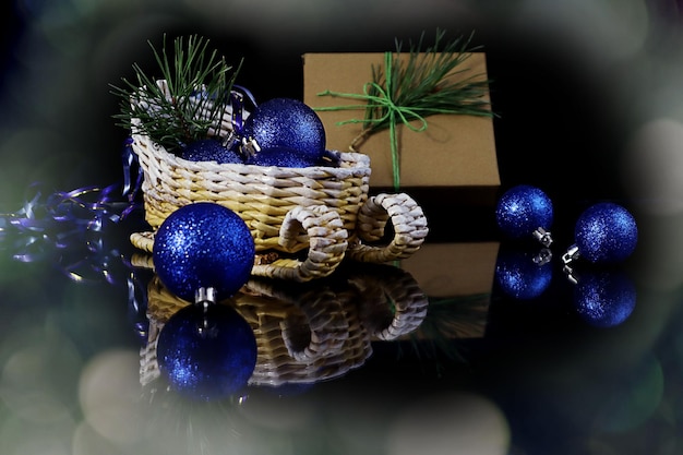 Traîneau décoratif de carte de Noël avec des boules bleues sur le fond d'un bokeh de fond foncé de cadeau emballé