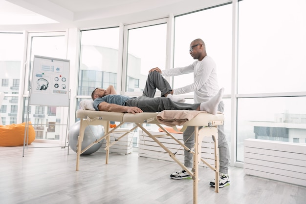 Traitement médical. Bel homme adulte allongé sur le canapé médical tout en faisant de la thérapie musculaire