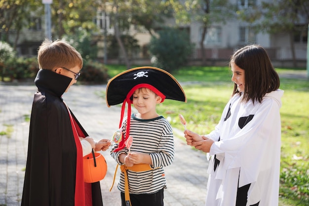 Traiter ou tromper Photo en plein air de trois enfants portant des costumes de carnaval pour Halloween partageant des bonbons les uns avec les autres Célébration des fêtes et concept de traditions d'Halloween