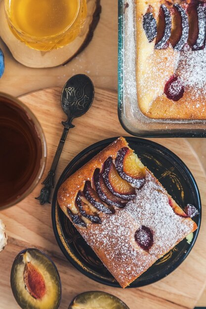 Une tranche carrée de tarte aux prunes sur une plaque antique noire miel d'acacia une cuillère à café vintage et une tasse de thé