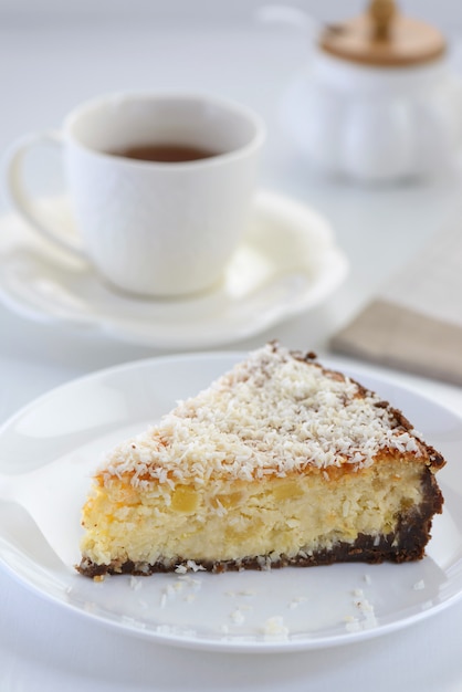 Une tranche de cheesecake à l'ananas et à la noix de coco et une tasse de thé sur la table.