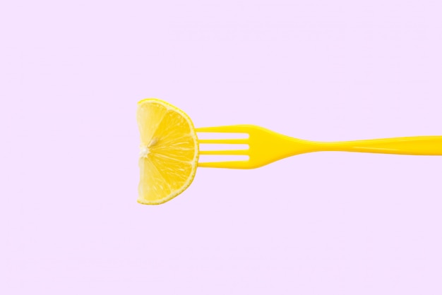 Tranche de citron dans une fourchette en plastique sur fond lilas pastel