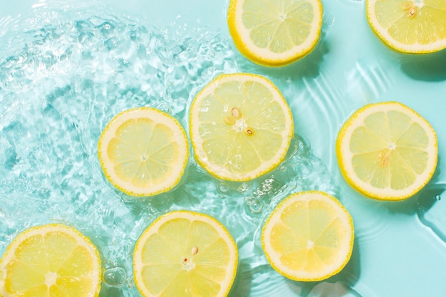 Tranche de citron sous l'eau ou dans l'eau avec des éclaboussures et des gouttelettes vue de dessus à plat sur fond bleu