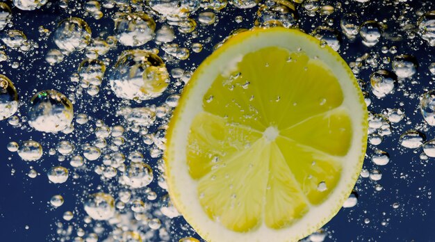 Photo tranche de citron sous l'eau dans de l'eau gazeuse ou de la limonade avec des bulles cocktail pétillant tonique rafraîchissant gros plan de citrons et de glaçons dans un verre citron vert dans des éclaboussures d'eau gazeuse boisson froide
