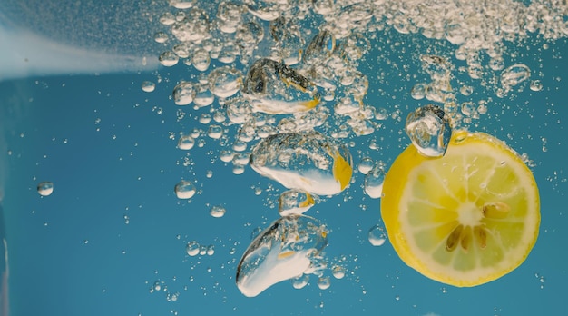 Tranche de citron sous l'eau dans de l'eau gazeuse ou de la limonade avec des bulles Cocktail pétillant tonique rafraîchissant Gros plan de citrons et de glaçons dans un verre Citron vert dans des éclaboussures d'eau gazeuse boisson froide