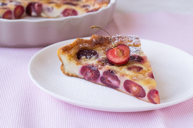 Tranche de clafoutis aux cerises sur assiette sur table rose