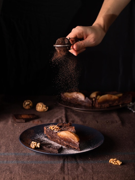 Photo une tranche de crostata au chocolat sur fond sombre, la main ajoutant du cacao sur le dessus