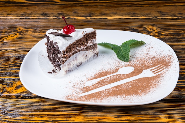 Photo tranche de délicieux gâteau au chocolat garnie d'une cerise et de menthe servie sur un plateau avec des détails décoratifs d'une fourchette et d'une cuillère en poudre de chocolat