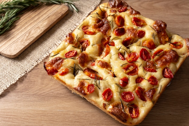 Tranche de focaccia avec romarin et huile d'olive et tomates sur table en bois