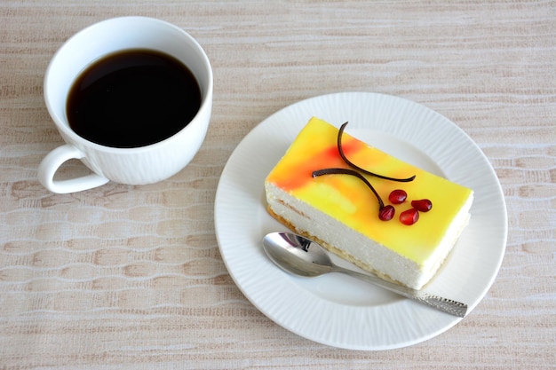 tranche de gâteau au fromage au citron sain isolé sur une soucoupe blanche avec une cuillère à café et une tasse de café