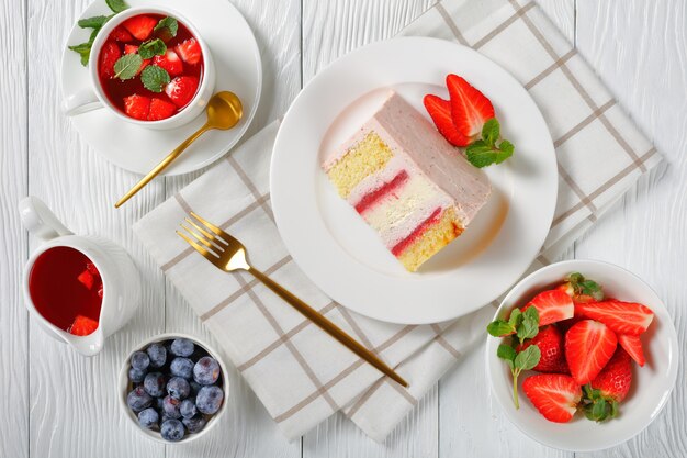 Une tranche d'un gâteau au fromage aux fraises rose servi avec des baies fraîches et de la limonade aux fraises sur une table en bois