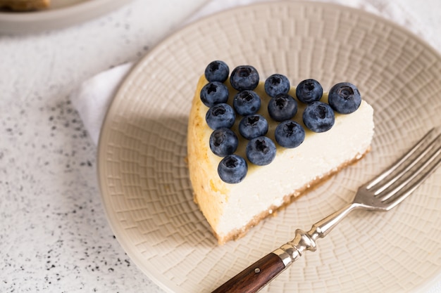 Tranche de gâteau au fromage classique de New York avec des bleuets sur une plaque blanche. Vue en gros plan. Boulangerie maison