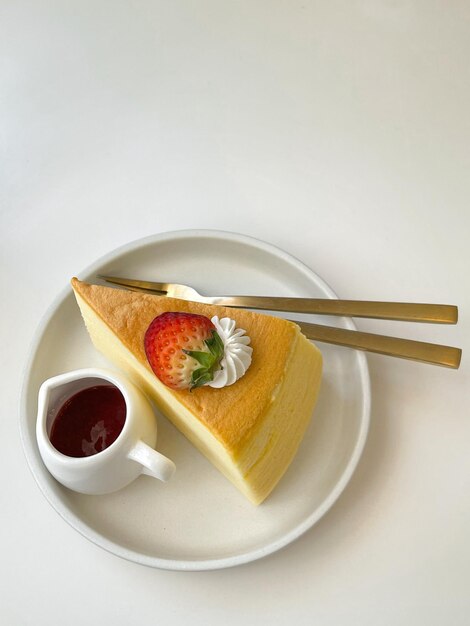 Une tranche de gâteau au fromage avec une fraise dessus et une tasse de café sur une assiette blanche.