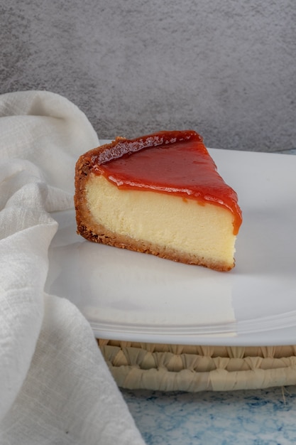 Photo tranche de gâteau au fromage avec de la pâte de goyave sur une plaque blanche sur fond gris et bleu.