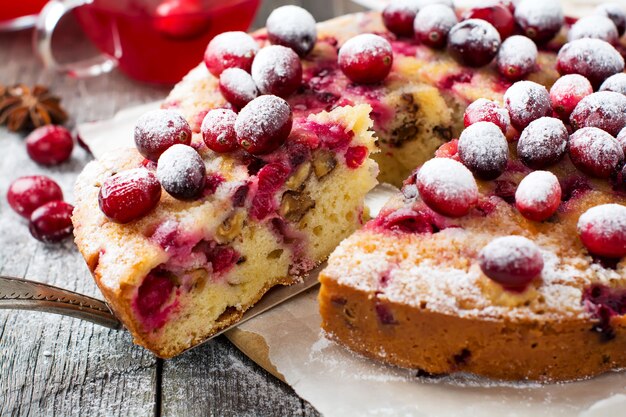 Tranche de gâteau aux canneberges maison avec des noix, des baies et du sucre en poudre sur le vieux bois fone