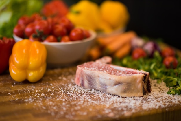 Tranche juteuse de steak cru avec des légumes autour sur une table en bois