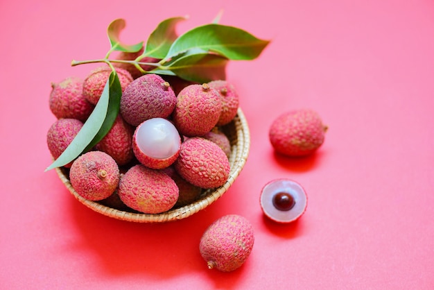 Tranche de litchi pelée sur fond rose rouge. Litchi frais avec des feuilles vertes récoltées dans le panier de l'été des fruits tropicaux en Thaïlande