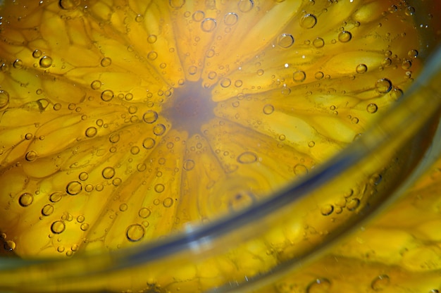 Une tranche d'orange recouverte de bulles se trouve dans un verre d'eau gazeuse. Fermer.
