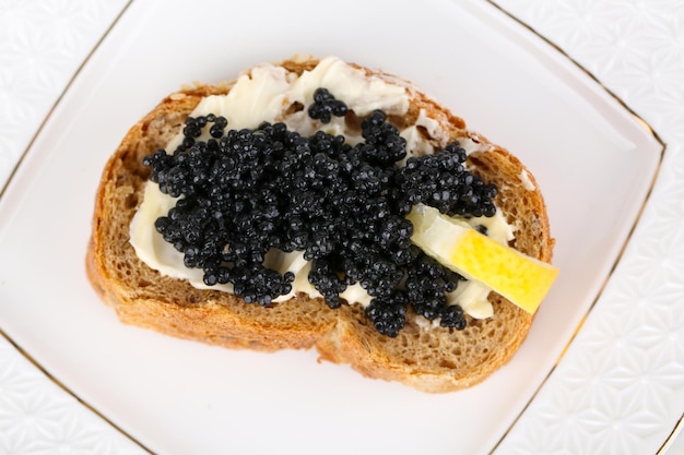 Tranche de pain avec du caviar noir au beurre et du citron sur le gros plan de la plaque