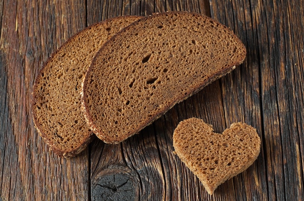 Tranche de pain noir et un morceau en forme de cœur sur bois