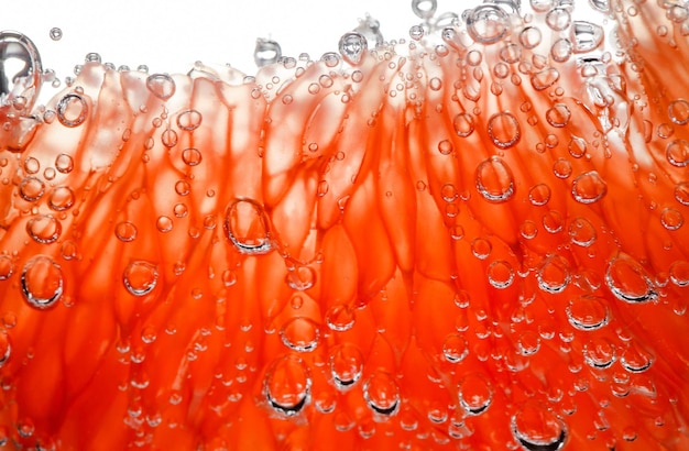 Photo tranche de pamplemousse pelées capsules pulpeuses dans l'eau avec des bulles d'air en arrière-plan lumière gros plan mise au point sélective