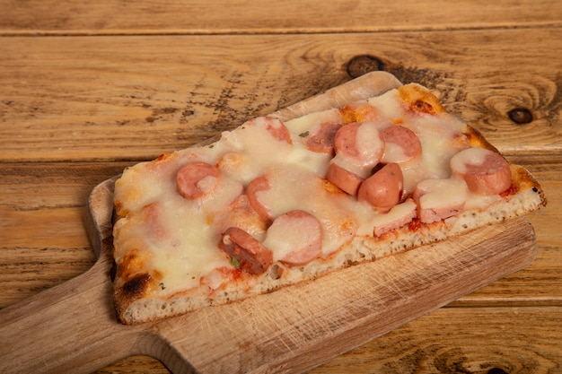 Tranche de pizza maison avec francfort sur une planche à découper en bois.