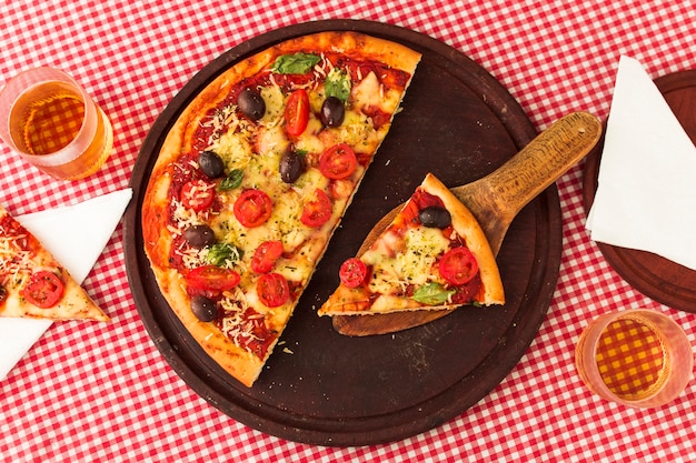 Tranche de pizza servie à la spatule sur un plateau circulaire en bois sur fond de nappe