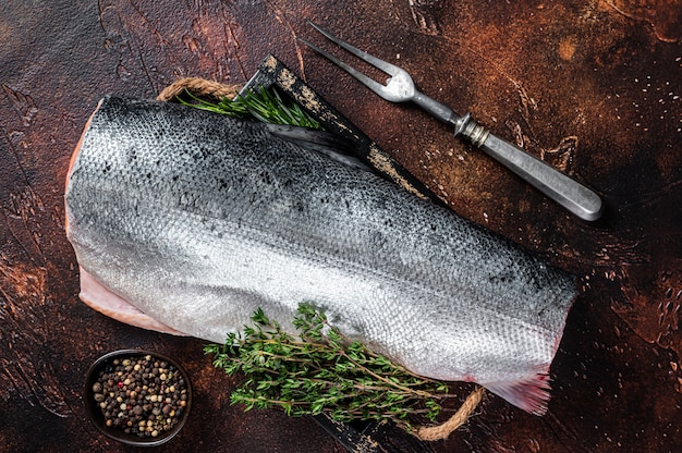 Tranche de poisson saumon coupé cru dans un plateau en bois avec du thym. Fond sombre.