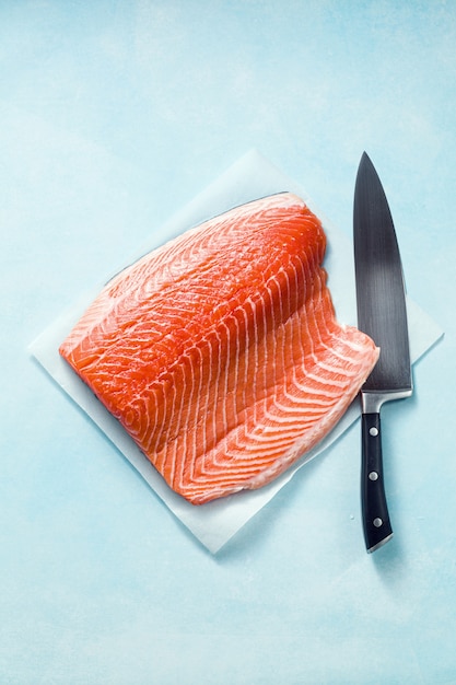 Tranche de saumon frais sur une planche à découper en bois avec un couteau de chef sur la table. recette de cuisine. fond de nourriture. produits de poisson frais