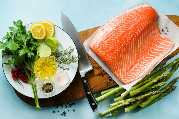 Tranche de saumon frais sur une planche à découper en bois avec des herbes aromatiques fraîches et des asperges sur la table. recette de cuisine. fond de nourriture. produits de poisson frais