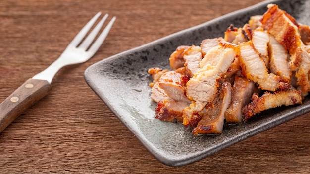 Tranche savoureuse de porc frit dans une assiette rectangulaire en céramique avec fourchette sur fond de texture de bois naturel rustique, rapport Full HD