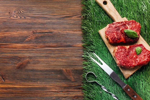 Photo tranche de steak cru sur une planche à découper en bois avec brochette métallique et fourchette sur tapis d'herbe