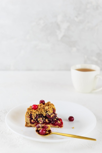 Une tranche de tarte aux canneberges sur une assiette blanche avec une tasse de thé sans gluten et sans lactose de sucre