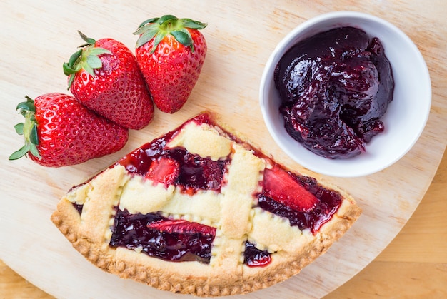 Tranche de tarte aux cerises maison et fraises sur table en bois