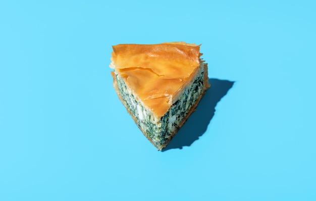 Tranche de tarte aux épinards minimaliste sur fond bleu Recette de tarte salée maison des Balkans