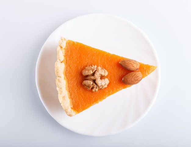 Une tranche de tarte à la citrouille douce américaine traditionnelle isolée sur une surface blanche.