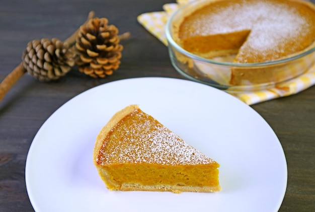 Une tranche de tarte à la citrouille maison avec une tarte entière floue pour le concept d'automne et de Thanksgiving