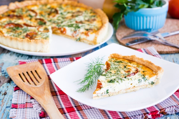 Tranche de tarte quiche française faite maison avec tomate, fromage et herbes sur une assiette