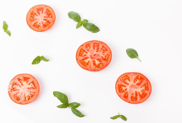 Tranche de tomate fraîche et brins de basilic fond végétal isolé sur blanc