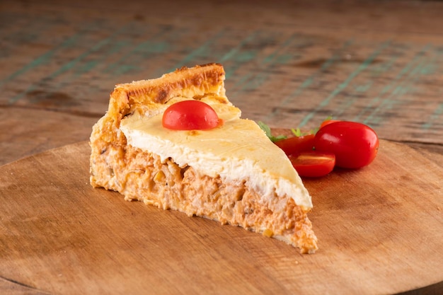 Tranche de tourte au poulet salée avec du fromage et des tomates cerises sur une planche ronde en bois sur un gros plan de table rustique