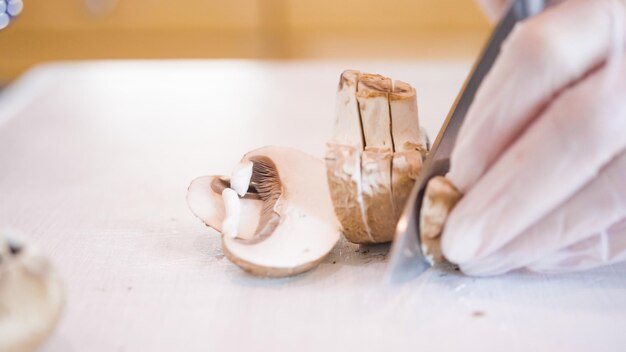 Trancher les champignons baby bella sur une planche à découper blanche.