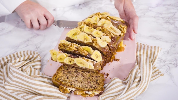 Trancher du pain aux bananes et aux noix garni de caramel et garni de chips de banane et de noix.