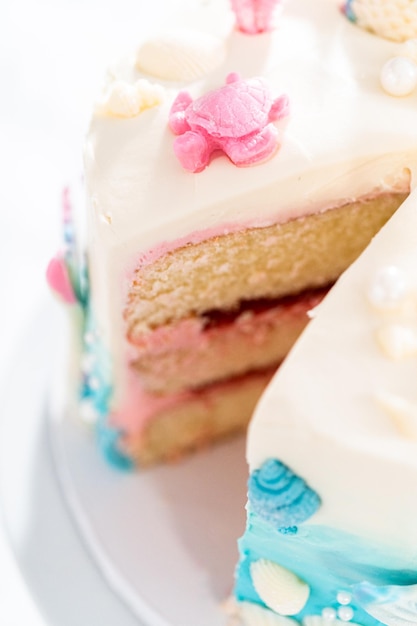 Trancher un gâteau à la vanille à 3 couches sur le thème de la sirène sur un présentoir à gâteaux.