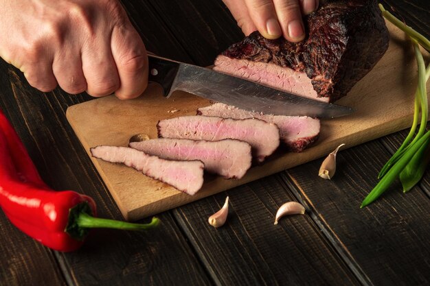 Trancher la viande cuite sur une planche de cuisine pour le dîner Gros plan d'un chef mains avec un couteau Aliments paysans