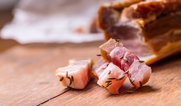 Tranches de bacon fumé cru sur planche de bois avec cumin et herbes.