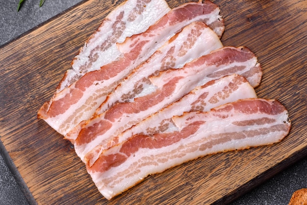 Photo tranches de bacon fumé cru sur une planche de bois avec des épices et des herbes