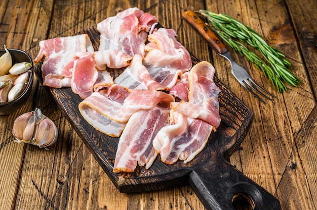 Tranches de bacon de porc fumé sur une planche à découper en bois. fond en bois. Vue de dessus.